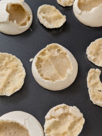 dark sheet covered with failed vegan macarons with gummy bottoms and crispy, hollow tops