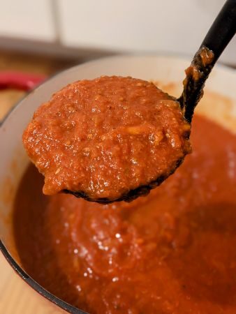 ladleful of tomato sauce hovering above a large pot of it