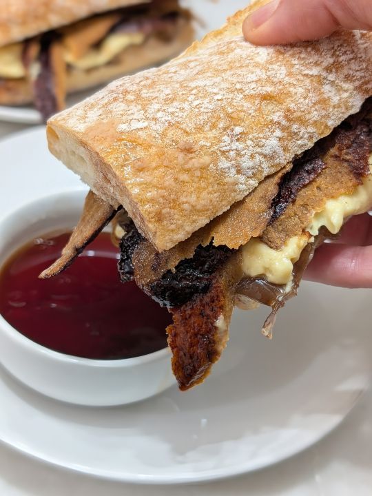 hand holding a dipped vegan French dip sandwich over a plate with a ramekin of jus