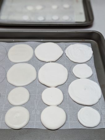 3 vertical rows of circular vegan royal icing transfers. The leftmost row without white food coloring is shiny