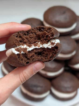 singular vegan whoopie pie missing a couple bites to show pillowy texture; a plate of others sits in the background