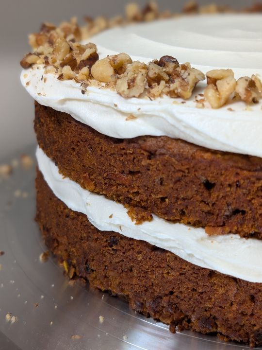 sideshot of vegan carrot cake with vegan cream cheese frosting in middle and on top, garnished with toasted chopped walnuts