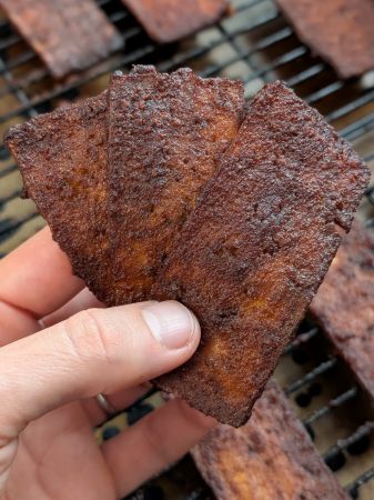 3 strips tofu jerky held in hand like a deck of cards, slightly leaning backward showing softer texture