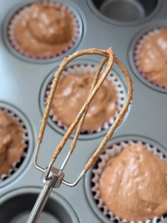 beater of vegan chocolate umami velvet cake batter above tray of unbaked cupcakes