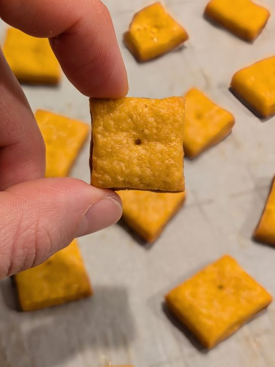 homemade vegan Cheez-It held above a lined baking tray of others