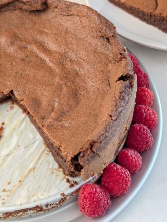 serving platter of vegan fallen chocolate souffle cake garnished with berries with a couple slices removed and placed in background